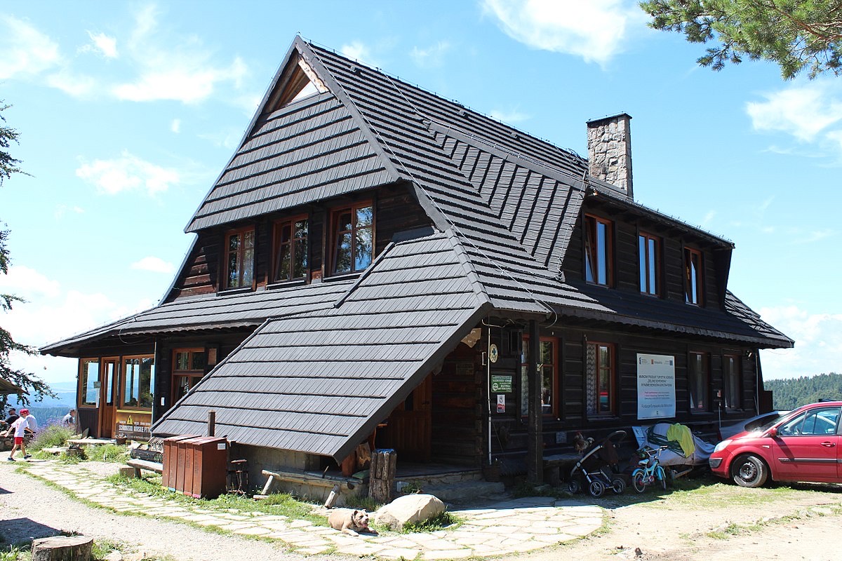 Drewniana bacówka PTTK nad Wierchomlą z czarnym dachem, latem, na polanie