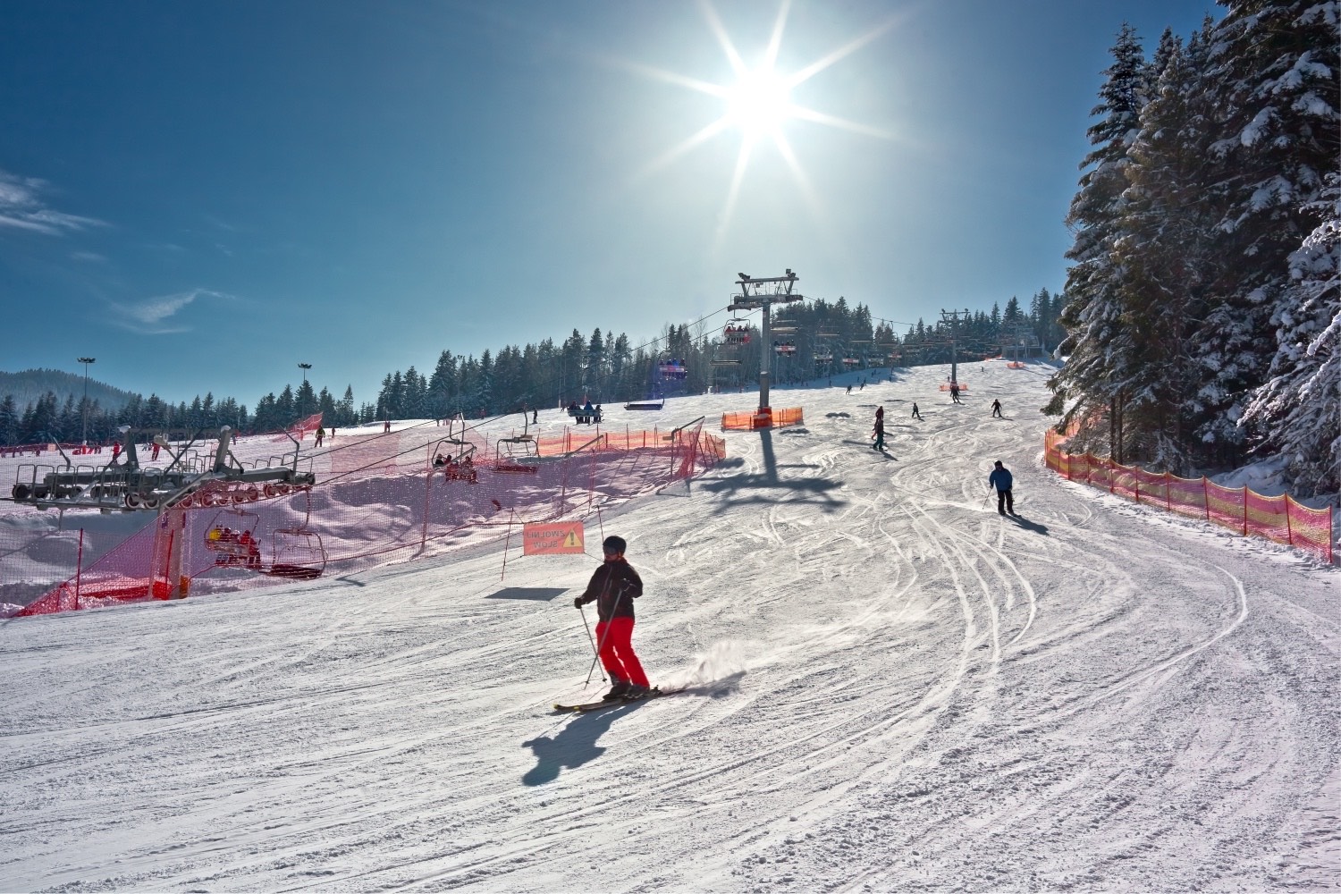 Stok narciarski TYLICZ.ski w słońcu, narciarz na trasie, wyciąg krzesełkowy i ośnieżone świerki